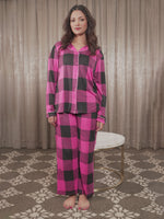 Woman wearing pink and black checkered pajamas standing against a beige curtain.