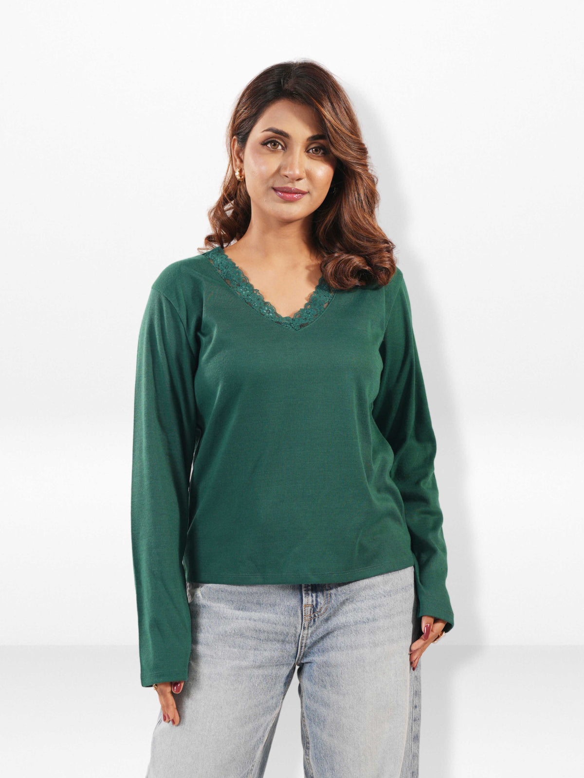 Woman wearing a green long-sleeve top and light blue jeans on a white background