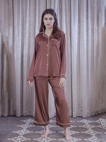 Woman wearing brown satin pajamas standing in front of a curtain.