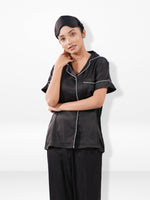 Woman wearing a black satin pajama set against a white background